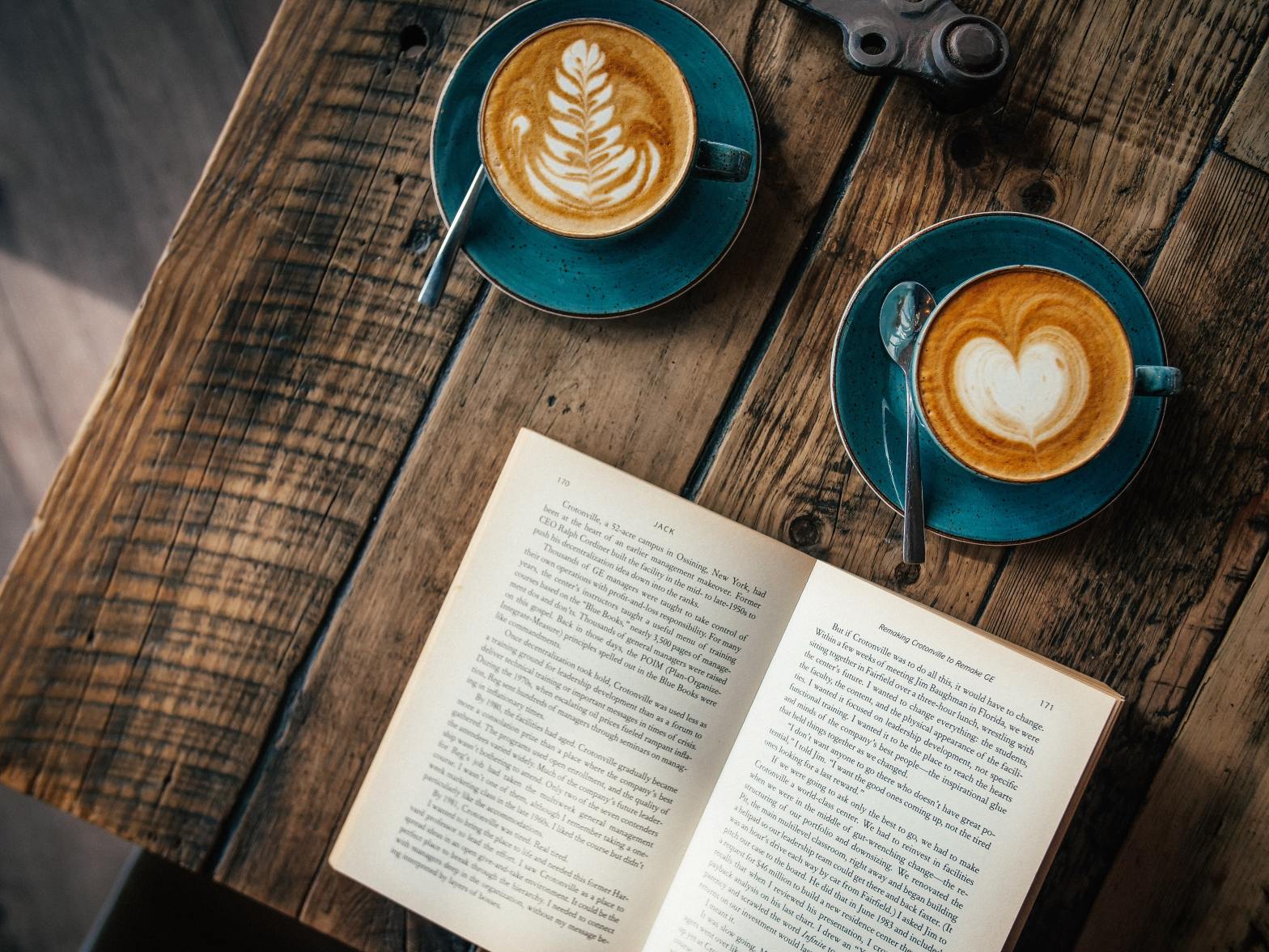 Two coffee cups on a wooden table, news to an open book