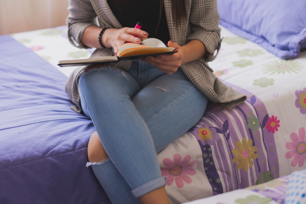 Woman reading on the bed in jeans and a blazer.