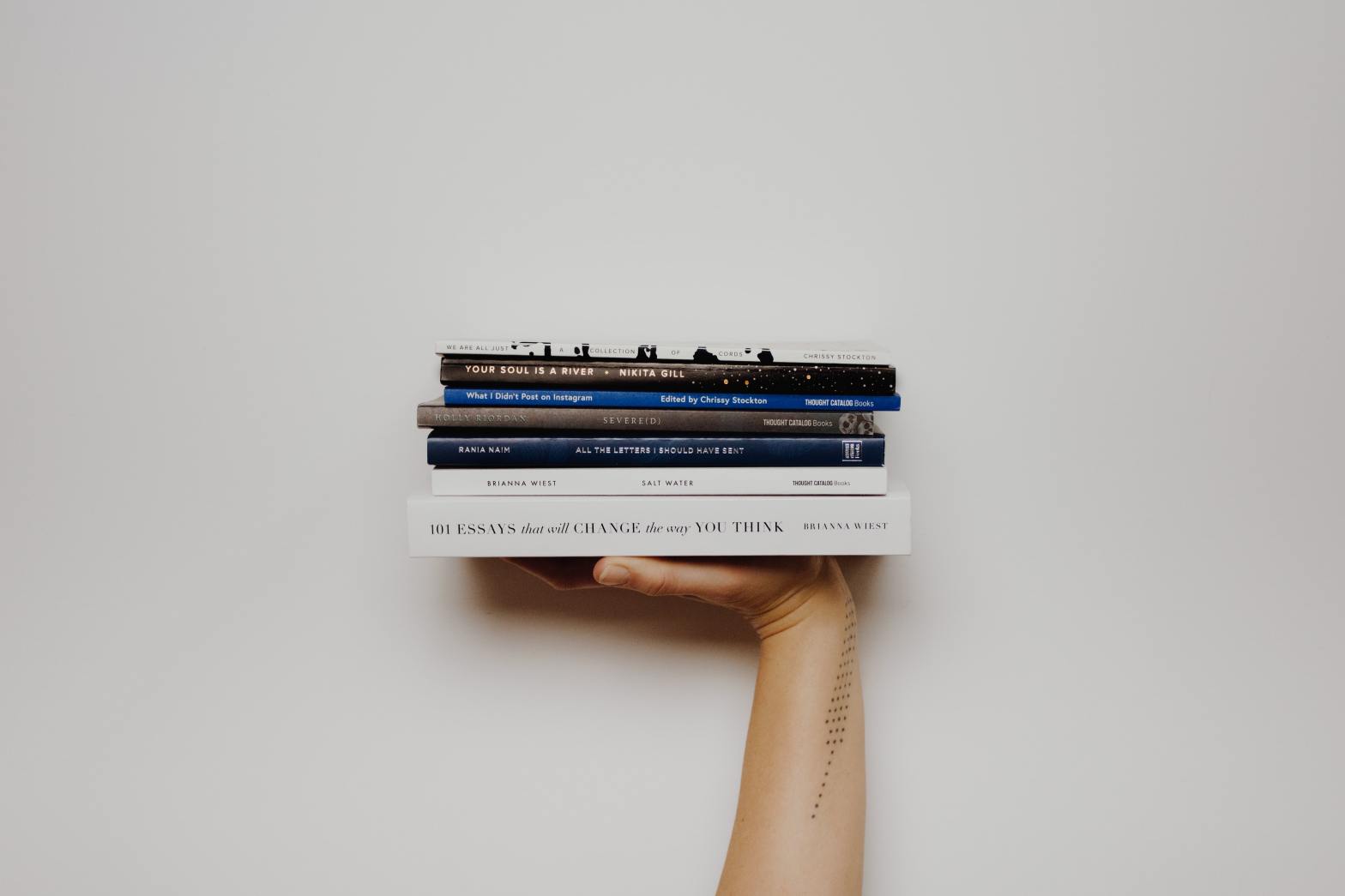 Hand holding stack of books against a white wall