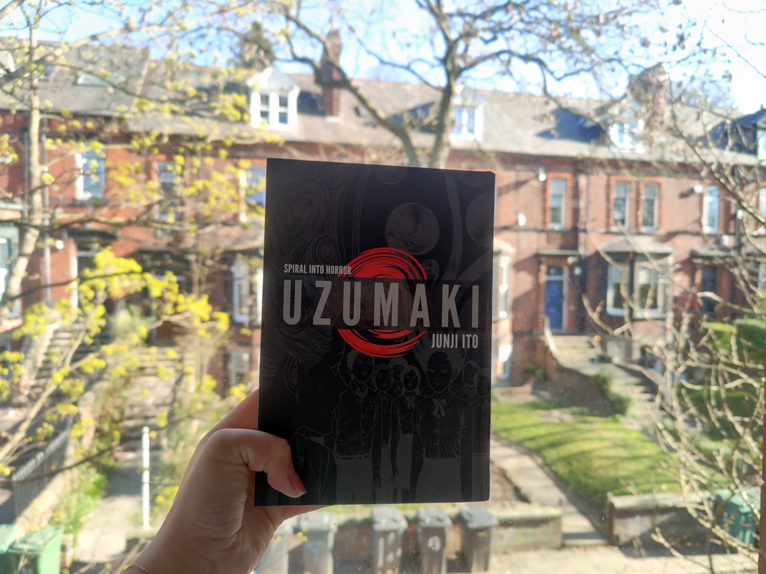 Uzumaki manga held against a bright window on a sunny day, with red-brick buildings in the background
