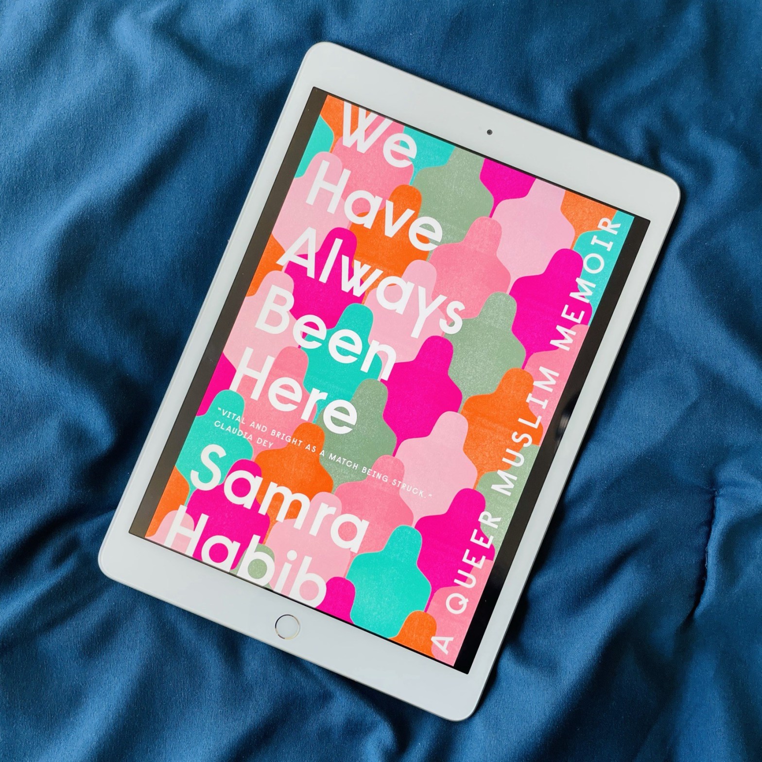 White e-reader on a satin navy fabric showing the cover of 'We have always been here', a queer Muslim memoir.
